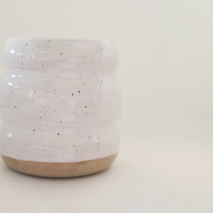 May include: A white ceramic mug with a textured, speckled glaze and a brown base.