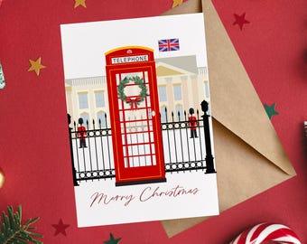 May include: A white greeting card featuring a red British telephone box with a green wreath, a Union Jack flag, and two guards in red uniforms standing behind a black iron fence. The text Merry Christmas is printed in red script at the bottom.