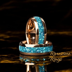 May include: Two rose gold rings with a band of turquoise-colored crushed stone. The rings are displayed on a reflective surface with the text "Riverstone Rings" in a cursive font.