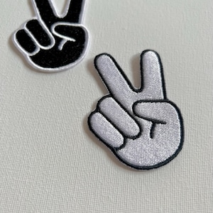 May include: Two peace sign patches, one black and one white. The patches are embroidered with a simple design of a hand making the peace sign.
