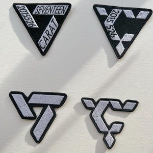 May include: Four embroidered patches featuring the logo of the K-pop group Seventeen. The patches are black and white with the group's name, "SEVENTEEN", and the fan club name, "CARAT", written in white. The patches are in the shape of a triangle and a stylized letter "S".