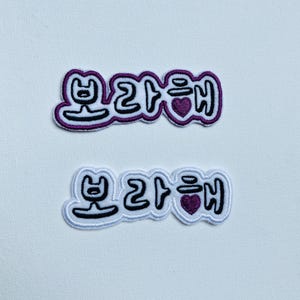 Peut inclure: Deux patchs en tissu blanc avec des broderies noires et violettes. Les patchs présentent le texte coréen "보라해" qui se traduit par "Je t'aime en violet".