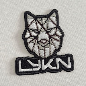Puede incluir: Parche bordado en blanco y negro con un diseño de lobo geométrico y la palabra "LYKN" en letras blancas.