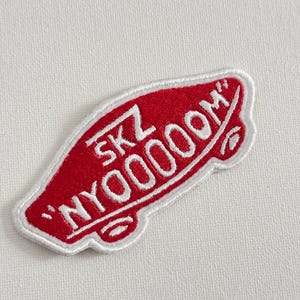 May include: Red embroidered patch with white stitching in the shape of a Vans shoe with the text "SKZ 'NYOOOOM'" on it.