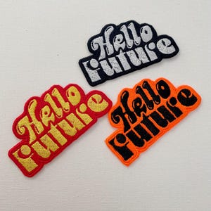 Könnte beinhalten: Drei gestickte Bügelbilder mit dem Text "Hello Future" in einer Retro-Schrift. Die Patches sind in Schwarz, Rot und Orange.