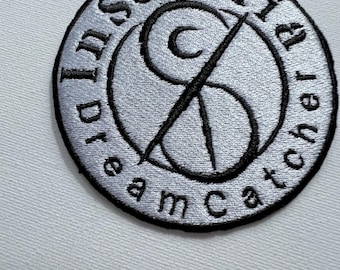 May include: A black and white embroidered patch with the text "Insomnia Dreamcatcher" in a circle around a stylized crescent moon and a cross.
