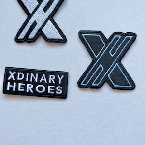 May include: Three embroidered patches, two black and white and one black with white lettering. The patches feature the letter "X" with a diagonal line through it. The black patch with white lettering reads "XDINARY HEROES".