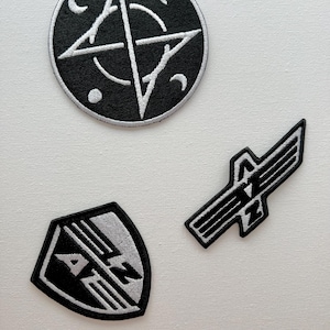 May include: Three black and white embroidered patches. One patch is a circle with a star in the centre and a circle around the star. The second patch is a shield shape with the letters "ANZ" in the centre. The third patch is a winged shape with the letters "ANZ" in the centre.