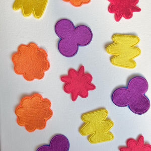 Puede incluir: Diez parches bordados de colores para planchar en diferentes formas, incluyendo una nube, una estrella, un zigzag y una flor. Los parches son de diferentes colores, incluyendo amarillo, naranja, rojo, morado y rosa.