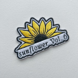 May include: A white embroidered patch featuring a yellow sunflower and the text "sunflower Vol. 6".