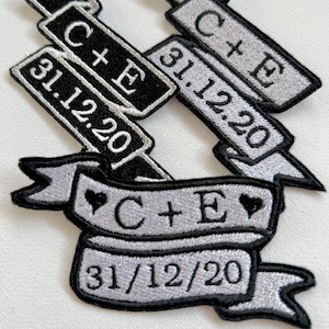 May include: Two embroidered patches with black and silver thread. The patches are shaped like banners and feature the text "C + E" and the date "31.12.20". One patch has a heart on either side of the text.