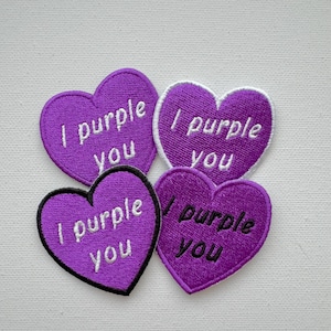 Peut inclure: Quatre patchs en forme de cœur violet avec une broderie blanche qui dit "I purple you".