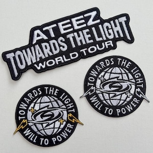 May include: Three black and white embroidered patches with the text "ATEEZ TOWARDS THE LIGHT WORLD TOUR" and a globe with lightning bolts and stars. The text "TOWARDS THE LIGHT WILL TO POWER" is on the globe.