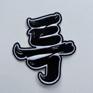 以下が含まれることがあります： スタイリッシュなフォントで「쿠」という単語が書かれた黒と白の刺繍パッチ