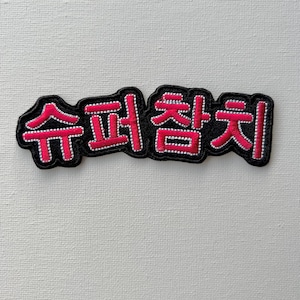 May include: A black and pink embroidered patch with the Korean text "슈퍼 춤치" which translates to "Super Dancer".