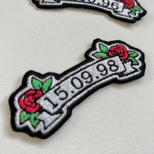 May include: Two white embroidered patches with black outlines and red roses. The top patch reads "08.09.96" and the bottom patch reads "15.09.98".