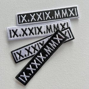 Könnte beinhalten: Vier gestickte Patches mit dem römischen Datumszahl "IX.XXIX.MMXI" in Schwarz und Weiß. Die Patches sind übereinander gestapelt, wobei der oberste Patch weiß mit schwarzen Buchstaben und der unterste Patch schwarz mit weißen Buchstaben ist.