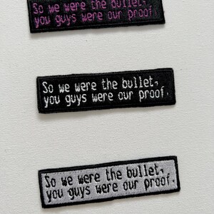 Può includere: Tre toppe ricamate in bianco e nero con il testo "So we were the bullet, you guys were our proof." Il testo è in bianco su sfondo nero sulle due toppe superiori e in grigio su sfondo nero sulla toppa inferiore.