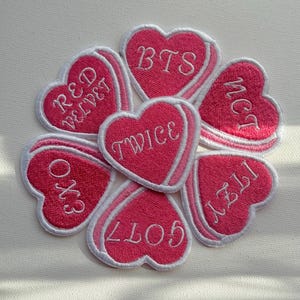 Peut inclure: Sept patchs en forme de cœur rose avec des contours blancs et du texte brodé blanc. Les patchs présentent les noms de groupes de K-pop populaires : BTS, TWICE, NCT, GOT7, EXO, RED VELVET.