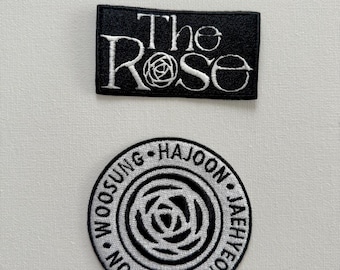 May include: Two black and white embroidered patches featuring the band "The Rose". The top patch has the band's name in white text with a white rose graphic. The bottom patch is a circle with the band's name in white text around the edge and a white rose graphic in the center.