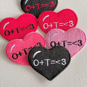 May include: Five felt heart-shaped patches with the text "O+T=<3" in white on a black background and red on a white background.