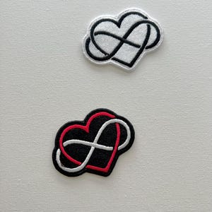 Peut inclure: Deux patchs brodés représentant un symbole d'infini entrelacé avec un cœur. Un patch est blanc avec des coutures noires, et l'autre est noir avec des coutures rouges et blanches.