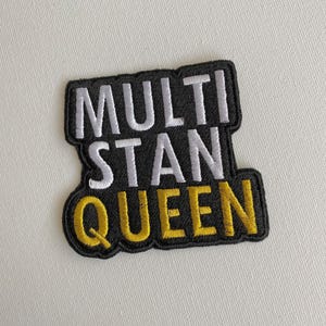 May include: Black embroidered patch with white and yellow lettering that reads "MULTI STAN QUEEN".