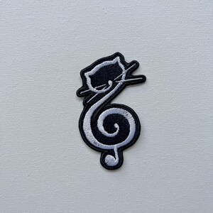 May include: Black and white embroidered iron-on patch of a cat curled into the shape of a treble clef.