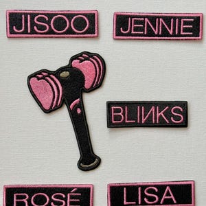 May include: Five black and pink embroidered patches with the names "JISOO", "JENNIE", "BLINKS", "ROSÉ", and "LISA". A black and pink embroidered patch of a hammer with a heart-shaped head is also included.