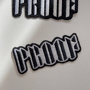 Könnte beinhalten: Zwei schwarze und weiße, gestreifte Bügelbilder mit dem Wort "PROOF" in einer fetten, stilisierten Schrift.