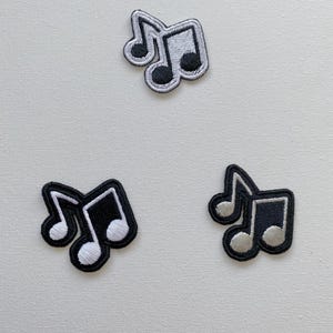 May include: Three iron-on patches featuring musical notes. Two patches are black with white musical notes, and one patch is white with black musical notes.