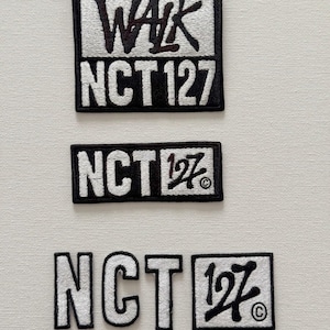 Puede incluir: Tres parches bordados con el texto "NCT 127" en letras blancas sobre fondo negro. El parche superior también tiene la palabra "WALK" en letras negras sobre fondo blanco. Los dos parches inferiores muestran el número "127" en una fuente estilizada.