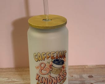 May include: A frosted glass tumbler with a bamboo lid and a clear straw. The tumbler features the text "Caffeine & Kindness Brew-tiful Blend" with a coffee cup graphic and floral accents. The tumbler is on a wooden surface.