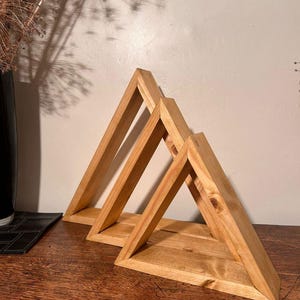 Può includere: Tre mensole triangolari in legno di diverse dimensioni. Le mensole sono realizzate in legno chiaro e sono disposte in fila. Sono progettate per essere montate a parete e offrono una soluzione di archiviazione decorativa.
