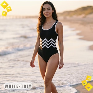 Puede incluir: Traje de baño negro con ribete blanco y diseño de zigzag blanco en la parte delantera. El traje de baño tiene un escote redondo. La persona lleva el traje de baño en la playa. El texto "WHITE-TRIM" está en la parte inferior de la imagen.