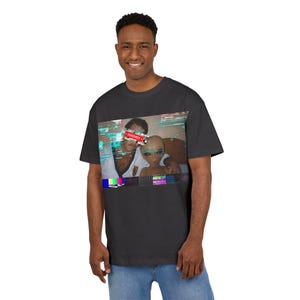 Könnte beinhalten: Dunkelgraues T-Shirt mit einer Grafik von zwei Personen, von denen eine wie ein Außerirdischer aussieht, mit einem roten "CENSORED"-Balken. Die Grafik hat einen Retro-Glitch-Art-Stil mit Farbbalken am unteren Rand. Das T-Shirt wird von einer Person getragen.