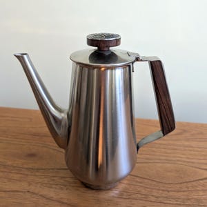 May include: A silver stainless steel coffee pot with a wooden handle and a decorative metal top.