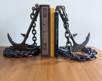 May include: Two antique-style bronze anchor bookends with black chains holding up three books. The books are "The Adventures of Sherlock Holmes" by Arthur Conan Doyle, "The Last Tycoon" by F. Scott Fitzgerald, and a yellow book titled "Eldridge 2023".