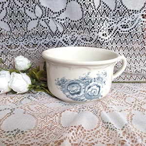 May include: White ceramic chamber pot with a blue floral design. The pot has a single handle on the side.