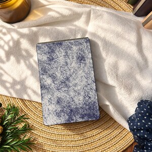 May include: A rectangular compact mirror featuring a white surface covered in a dense, dark blue scribbled or tangled line pattern. The object has a metallic frame and a smooth, flat top surface, presenting a distinct contrast between the dark lines.