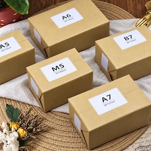 May include: Five rectangular cardboard boxes in a light brown kraft finish, each featuring a white label with black text indicating sizes A5 148*105mm, A6 105*148mm, B7 88*125mm, M5 74*105mm, and A7 80*127mm, arranged on a textured woven surface.