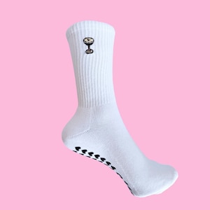 Könnte beinhalten: Weiße gerippte Sportsocken mit einem kleinen, gestickten Cocktailglas-Design. Die Socken haben schwarze herzförmige Griffe auf der Sohle. Die Socken sind aus einem weichen, bequemen Material.