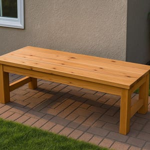 Może przedstawiać: Prostokątna drewniana ławka z naturalnym wykończeniem. Ławka ma listwowy blat i solidne nogi. Ma około 152 cm długości, 46 cm szerokości i 46 cm wysokości. Idealna do siedzenia na zewnątrz.