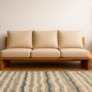 Könnte beinhalten: Ein modernes Holzsofa mit drei beigefarbenen Kissen und einem passenden Holzsockel. Das Sofa steht in einem Raum mit neutraler Farbgebung, einem gemusterten Teppich und einer Topfpflanze. Das Sofa ist etwa 183 cm lang.