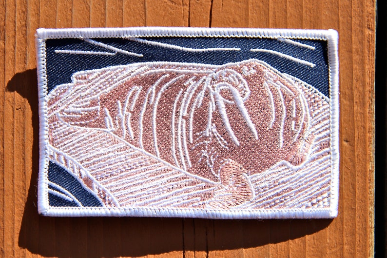 May include: White embroidered patch of a walrus with its tusks showing, on a dark blue background. The patch has a white border.