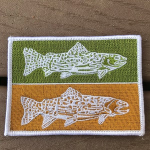 Pode incluir: Um remendo bordado branco com dois peixes, um em um fundo verde e outro em um fundo dourado. Os peixes s&atilde;o estilizados e t&ecirc;m um padr&atilde;o detalhado.