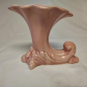 May include: A pink ceramic vase shaped like a trumpet with a curled base.