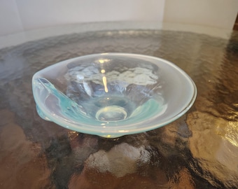 May include: A clear glass bowl with a light blue iridescent finish. The bowl has a wavy, organic shape and a slightly raised center.