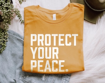 May include: A mustard yellow t-shirt with the text "PROTECT YOUR PEACE" printed in white.
