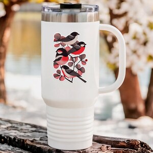 A beautiful and minimal illustration of four finches perched in a tree. Design is black, red and cream, printed on a kiss-cut vinyl sticker with a white border. Sticker is shown on a tall white tumbler in a luxurious outdoor setting.